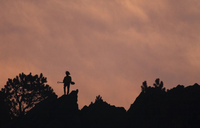 A firefighter stands on a ridge above Linden as Saturday's sunrise colors the smoke from a Boulder foothills fire.