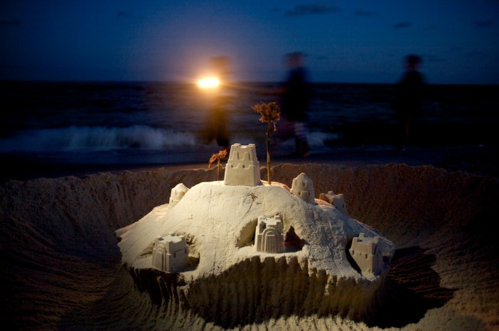 Beachgoers shine their flashlight as they walk by a giant sand castle creation as evening falls in Orange Beach, Ala., Wednesday, June 11, 2008.