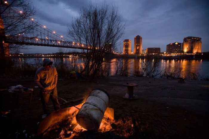 Harry Shoup and Terry hang out at a homeless camp on the banks of the Ohio River in Cincinnati, Ohio, Sunday evening, March 5, 2006, with the Covington, Ky., skyline in the background. A brief rain and snow storm had just passed, so the men placed a plastic barrel on the fire at regular intervals so the plastic would keep the fire going even with the moisture. Shoup said he served 25 years in prison after being charged as an accessory to murder. Terry said he was a military veteran who had fought in the Gulf War.